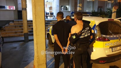 Un policía local con el uniforme roto lleva esposado a uno de los detenidos en Sevilla.