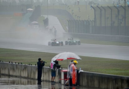 Hulkenberg y Kobayashi ruedan en Shanghái mientras unos fotógrafos se protegen de la lluvia.