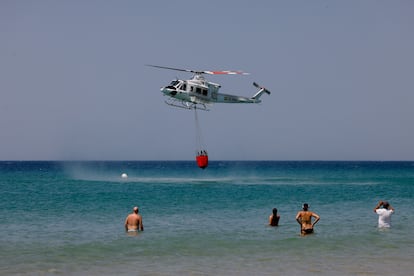 La gente se baña en la playa de Atlanterra mientras una de las aeronaves de Infoca cargan agua para apagar el incendio de la Sierra de la Plata, en Tarifa