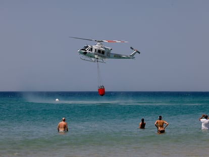 La gente se baña en la playa de Atlanterra mientras una de las aeronaves de Infoca cargan agua para apagar el incendio de la Sierra de la Plata, en Tarifa