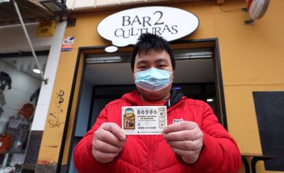 Juan, propietario del bar Dos Culturas de Zaragoza, muestra uno de los décimos agraciados con el quinto premio 86986.