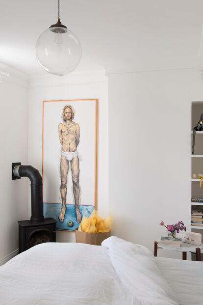 El pintor Ian Bruce firma el desnudo junto a la cama del dormitorio, al lado de la estufa de gas. La mesilla es de Heal’s, y la lámpara, de Lighting Direct. 