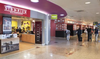 Un grupo de pasajeros pasa ante una tienda y un restaurante en la zona de embarque de la T1 de Madrid-Barajas.