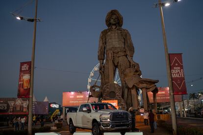 En la entrada del rodeo se observa la estatua metálica de un vaquero de 27 metros de altura y 170 toneladas de peso, rodeada por puestos de carne asada y comercios ofreciendo productos para los asistentes. 