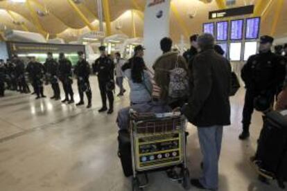 Varios viajeros miran las pantallas de vuelos, junto a un cordón policial, en la T4 del aeropuerto de Barajas, en la primera de las 15 jornadas de huelga convocadas por los trabajadores contra el Plan de Reestructuración de la aerolínea. EFE/Archivo