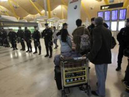 Varios viajeros miran las pantallas de vuelos, junto a un cordón policial, en la T4 del aeropuerto de Barajas, en la primera de las 15 jornadas de huelga convocadas por los trabajadores contra el Plan de Reestructuración de la aerolínea. EFE/Archivo