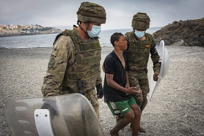 Dos soldados del Ejército de Tierra acompañan a un menor que acaba de salir del agua tras cruzar la frontera nadando.