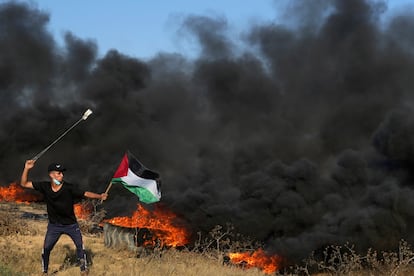 A Palestinian protester uses sling shots to hurls stones while waves Palestinian flag as others burn tires during clashes with Israeli security forces along the frontier with Israel, east of Gaza City, Friday, Sept. 22, 2023.