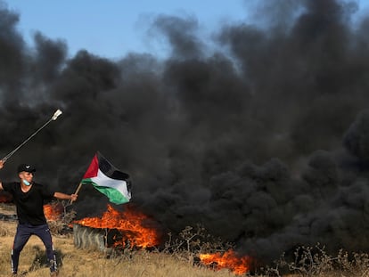 A Palestinian protester uses sling shots to hurls stones while waves Palestinian flag as others burn tires during clashes with Israeli security forces along the frontier with Israel, east of Gaza City, Friday, Sept. 22, 2023.