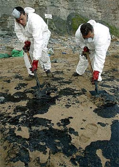 Dos trabajadores de Tragsa limpian fuel en la playa de Peñarrubia.