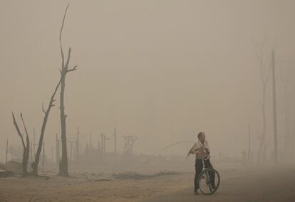 Un hombre camina, con su bicicleta, en el pueblo de Keltsy. Los distintos fuegos a lo largo del país se han cobrado la vida de 48 personas en la última semana.