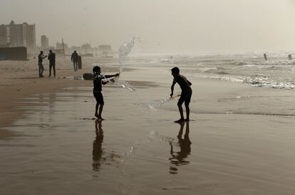 Niños palestinos juegan con botellas de agua en un día de tormenta de arena en una playa de Gaza.