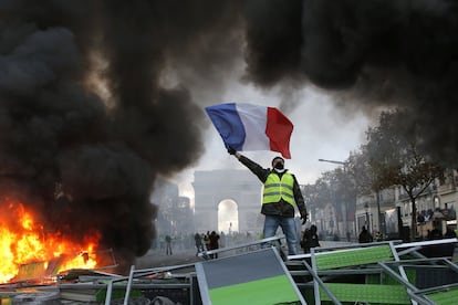 Un manifestante ondea la bandera de Francia mientras participa en la protesta de los 'chalecos amarillos' en París (Francia), el 24 de noviembre de 2018. Al fondo de la imagen, el Arco de Triunfo. Con una agenda inicial que buscaba la supresión del aumento de la tasa al diésel y la gasolina, prevista para el 1 de enero, la revuelta consiguió que el Gobierno francés anulase la subida de la tasa al carburante y aprobase ayudas de 10.000 millones de euros para reforzar el poder adquisitivo.