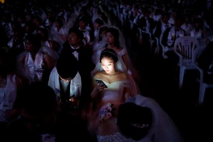 Una mujer consulta su teléfono durante la ceremonia en una boda multitudinaria en Corea del Sur, celebrada por la Iglesia de la Unificación en la que se han casado cerca de 4.000 personas