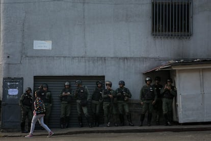 Membros da Guarda Nacional Bolivariana (GNB) esperam em um muro enquanto um grupo de pessoas se manifesta em uma rua nas proximidades de um comando da Guarda Nacional Bolivariana, em Caracas (Venezuela).