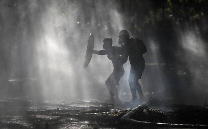 Manifestantes se escudan del rocío de un cañón de agua de la policía que intenta dispersarlos en Santiago, Chile.