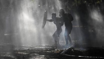 Manifestantes se defendem dos jatos d’água com os quais a polícia tenta dispersá-los, durante um protesto em Santiago.