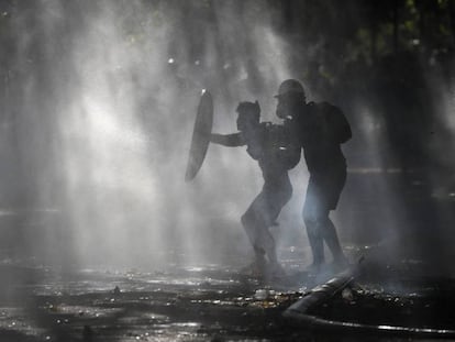 Manifestantes se defendem dos jatos d’água com os quais a polícia tenta dispersá-los, durante um protesto em Santiago.