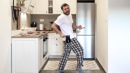 Un hombre bailando en la cocina de su casa con el pijama puesto mientras se prepara un café