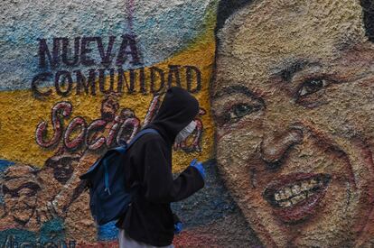 Un hombre con máscaras y guantes protectores pasa por delante de un mural que representa a Hugo Chávez, en el barrio de La Vega en Caracas, el pasado 28 de julio.