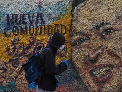 Un hombre con máscaras y guantes protectores pasa por delante de un mural que representa a Hugo Chávez, en el barrio de La Vega en Caracas, el pasado 28 de julio.