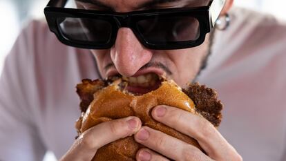 Un hombre se come una hamburguesa en un local de comida rápida en Milán (Italia).