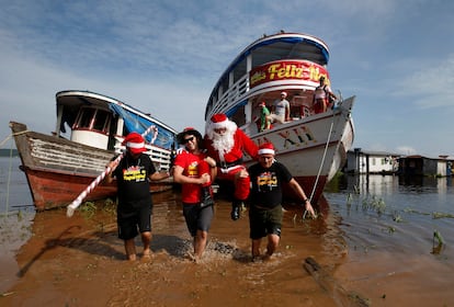 Jorge Barroso, vestido de Pap Noel, es transportado por sus ayudantes tras llegar en un barco para distribuir regalos a los ni?os que viven en las comunidades ribere?as del Amazonas, en Iranduba, Brasil.