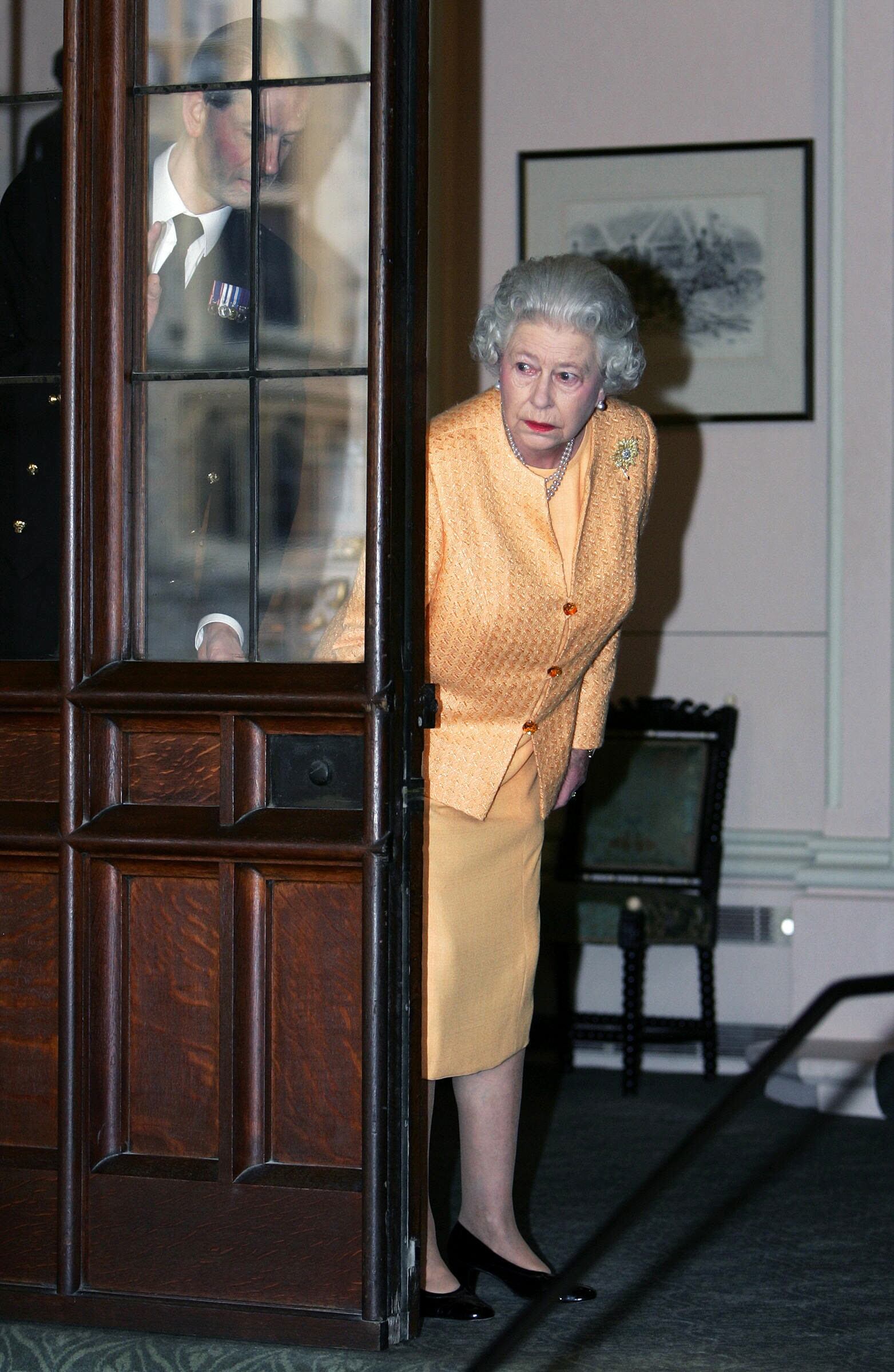 La reina Isabel II y su ayudante, Paul Whybrew, miran tras una puerta para revisar la limusina que espera al presidente francés Jacques Chirac y su esposa para partir del castillo de Windsor, el 19 de noviembre de 2004.