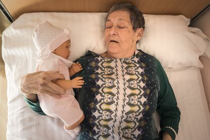 Mari Fe Lorente abraza a uno de los muñecos, tumbada en una cama. Para ella la terapia es especialmente relevante a la hora de dormir, siempre le dan un muñeco, cuenta el personal del centro.