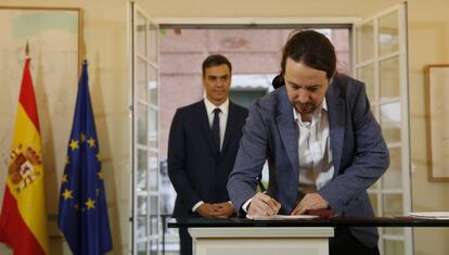 Detrás, el presidente del Gobierno, Pedro Sánchez,observa como el secretario general de Podemos, Pablo Iglesias, la firma el acuerdo presupuestario para 2019
 