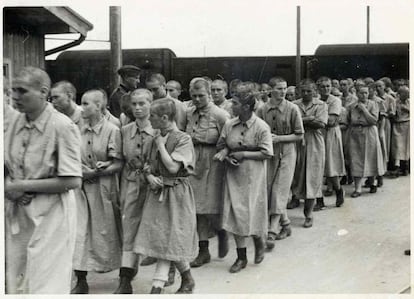 Prisioneiras entram no campo de mulheres, já com o uniforme de prisioneiras, sob o olhar de um guarda da SS.