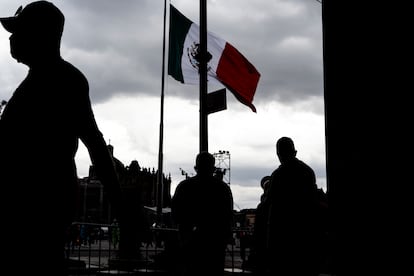 Tres hombres caminan frente a la bandera mexicana en la Plaza de la Constitución, también llamada Zócalo, en el Centro Histórico de Ciudad de México.