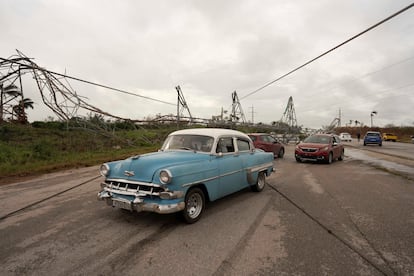 Automóviles pasan cerca de postes eléctricos caídos en una carretera en Artemisa, Cuba.