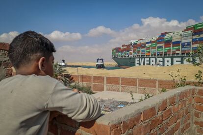 Un niño observa el buque desde una población cercana al canal de Suez, este jueves. Royal Boskalis Westminster, la empresa a quienes los propietarios del 'Ever Given' ―la compañía japonesa Shoei Kisen Kaisha― han encargado el rescate de la nave, tan solo ha podido precisar que se necesitarán “varios días o incluso semanas” para liberar el canal.