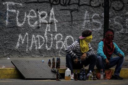 Dos hombres encapuchados permanecen sentados junto a una pintada donde se lee 'Fuera Maduro', en una calle de Caracas (Venezuela).