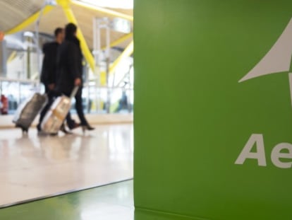 Dos viajeros pasan ante un &#039;stand&#039; de Aena en el aeropuerto madrile&ntilde;o de Barajas.