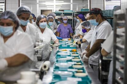 La cocina del hospital pasó de servir 600 comidas a 1.300 durante la primera ola del coronavirus. Para alimentar a las personas que aguardaban en Urgencias y que estaban en sillones, improvisaron la entrega de bolsas de pic-nic. Llegaron a repartir 300. En la imagen el equipo prepara las bandejas el pasado 5 de marzo. Al fondo, la coordinadora de gobernantas Antonia Muriel.