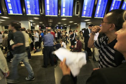 Pasajeros en el aeropuerto de Barajas observan la información de los vuelos retrasados por la erupción de un volcán en Islandia.