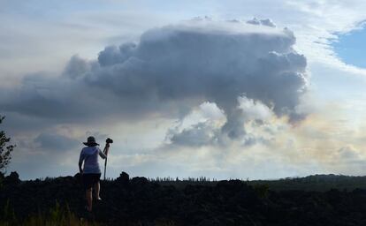 Un hombre sube a un flujo de lava petrificada de una antigua erupción para obtener una imagen de la columna de humo volcánico en la distancia sobre el área de Leilani Estates, cerca de Pahoa, Hawái, el 6 de mayo de 2018.