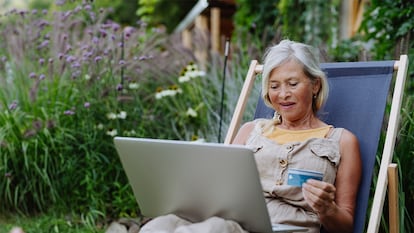 una mujer comprando online desde el ordenador en el jardín de su casa.