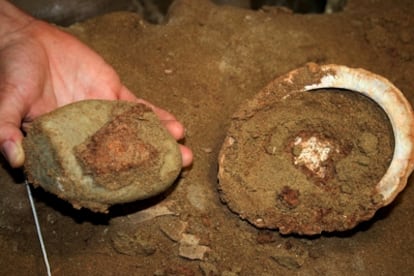 Una concha con ocre rojo en su interior, a la derecha, y la piedra de moler extraída de la misma.