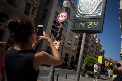 Una mujer hace una foto con el móvil a un termómetro que marca 42 grados en una calle de Granada, en julio de 2018.