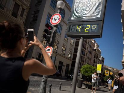 Una mujer hace una foto con el móvil a un termómetro que marca 42 grados en una calle de Granada, en julio de 2018.
