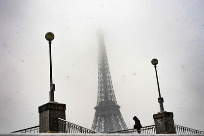 Una mujer atraviesa un puente sobre el río Sena con la Torre Eiffel al fondo.