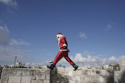 Un palestino disfrazado de Santa Claus camina sobre la pared de la ciudad vieja de Jerusalén repartiendo árboles de Navidad.