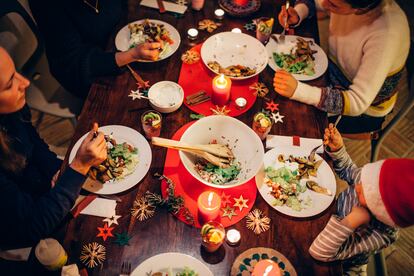 Una familia come alrededor de una mesa decorada con motivos navideños.