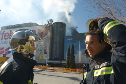 Agentes de bomberos ante el centro comercial vecino al edificio Windsor.