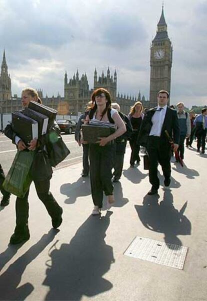 Un grupo de peatones cruza el puente de Westminster, junto al Parlamento, portando efectos personales y de trabajo.