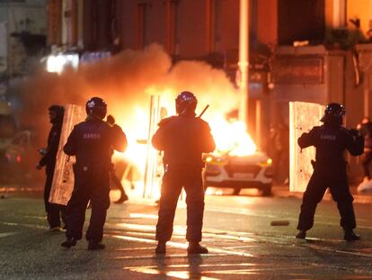 A car burns as Irish policemen stand at the scene of an attack in Dublin city centre, Thursday Nov. 23, 2023.