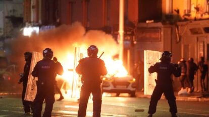 A car burns as Irish policemen stand at the scene of an attack in Dublin city centre, Thursday Nov. 23, 2023.